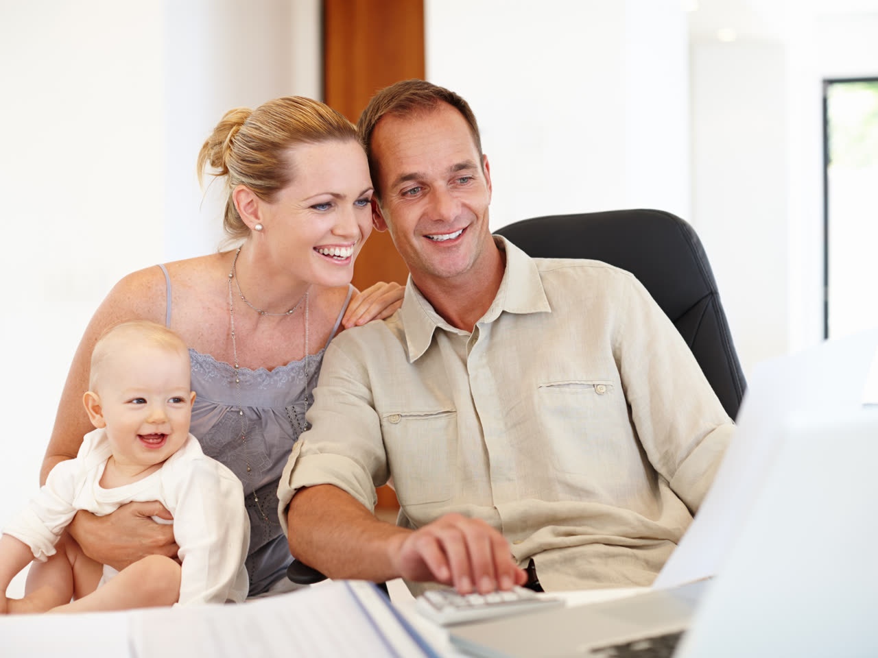 Young parents reviewing their family budget on a laptop while holding their baby at home